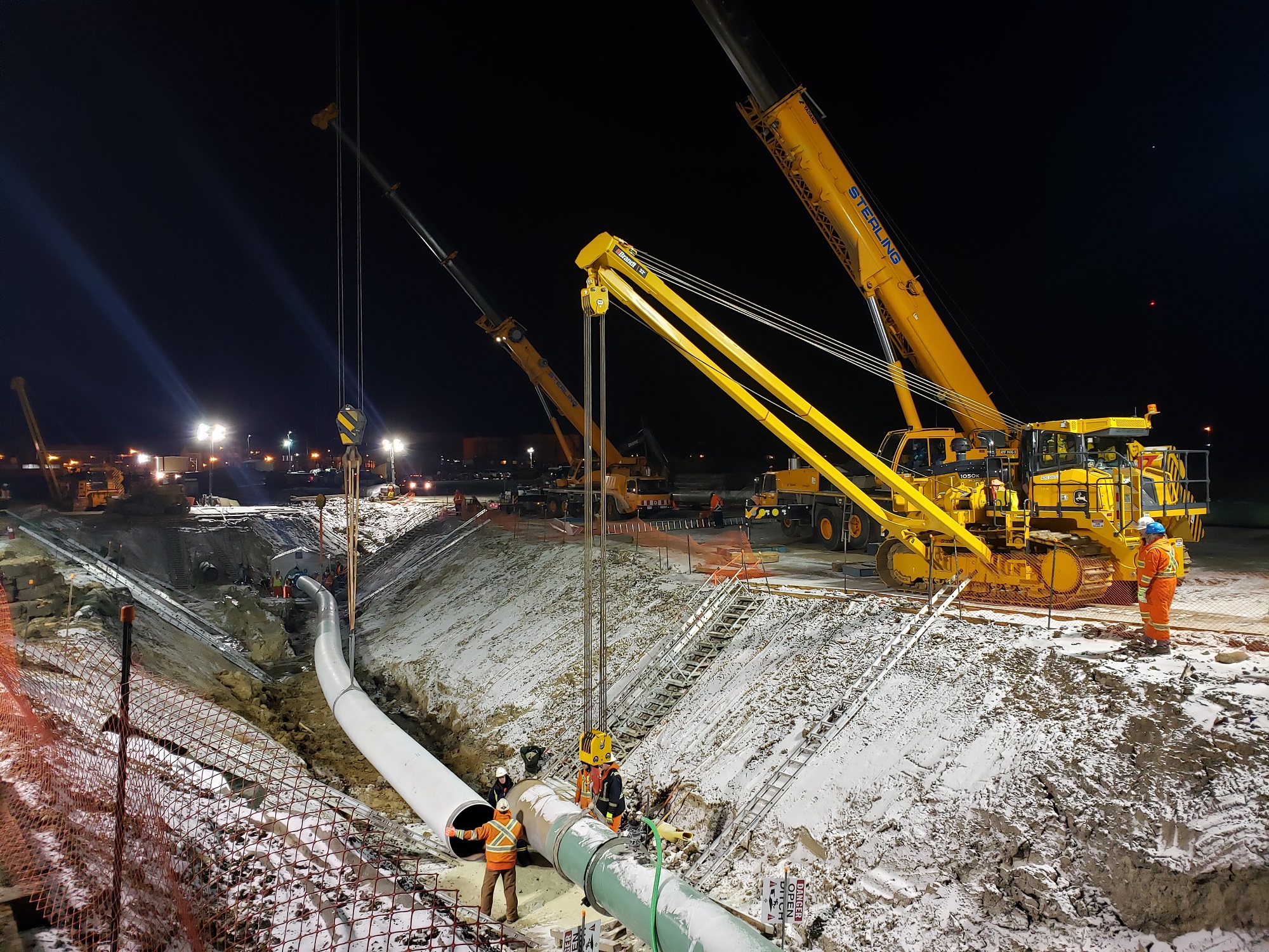 Cranes lowering pipe into trench